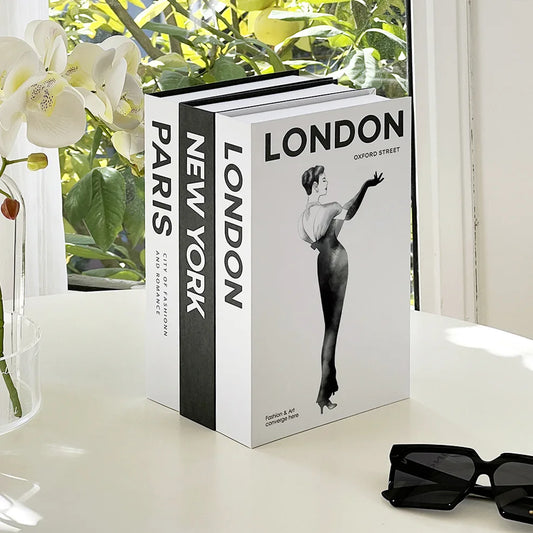 Three books titled 'Paris', 'New York', and 'London' on a table with sunglasses and flowers.