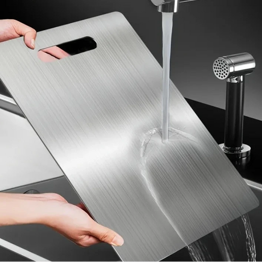 Person washing a metal cutting board under running water in a kitchen sink.