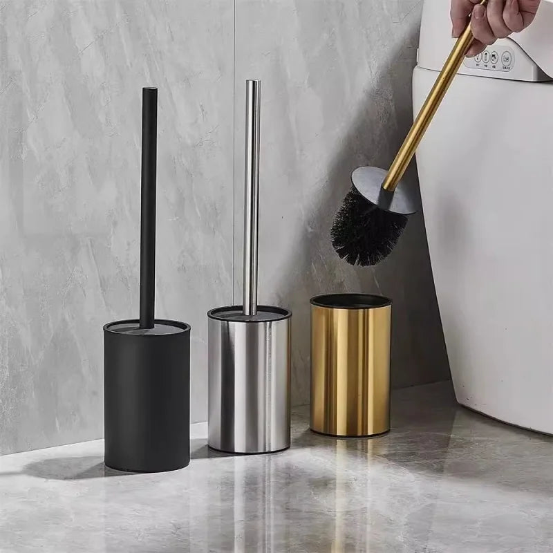 Three toilet brushes in black, silver, and gold stands on a bathroom floor.