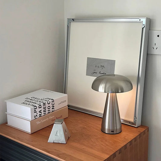 Silver table lamp on a wooden surface with books and a decorative item in the background.